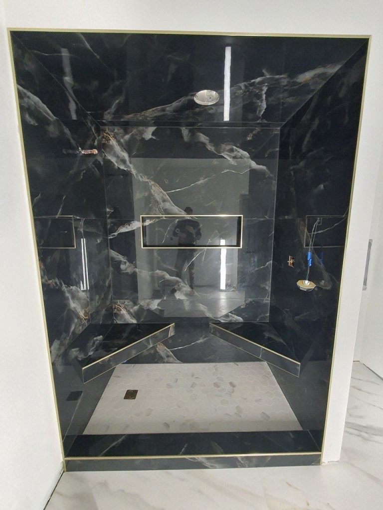 Finished walk-in shower clad in black marble-look porcelain with brass inlay trim and a hexagon mosaic floor.