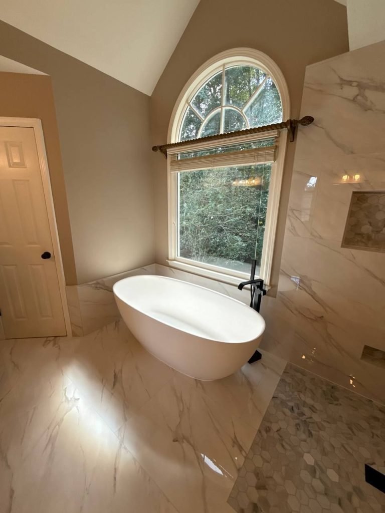 Freestanding soaking tub with a matte black floor filler beneath a large arched window.