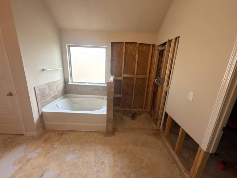Dated bathroom mid-demolition with a corner tub, travertine tile and the shower stripped to the sheathing.