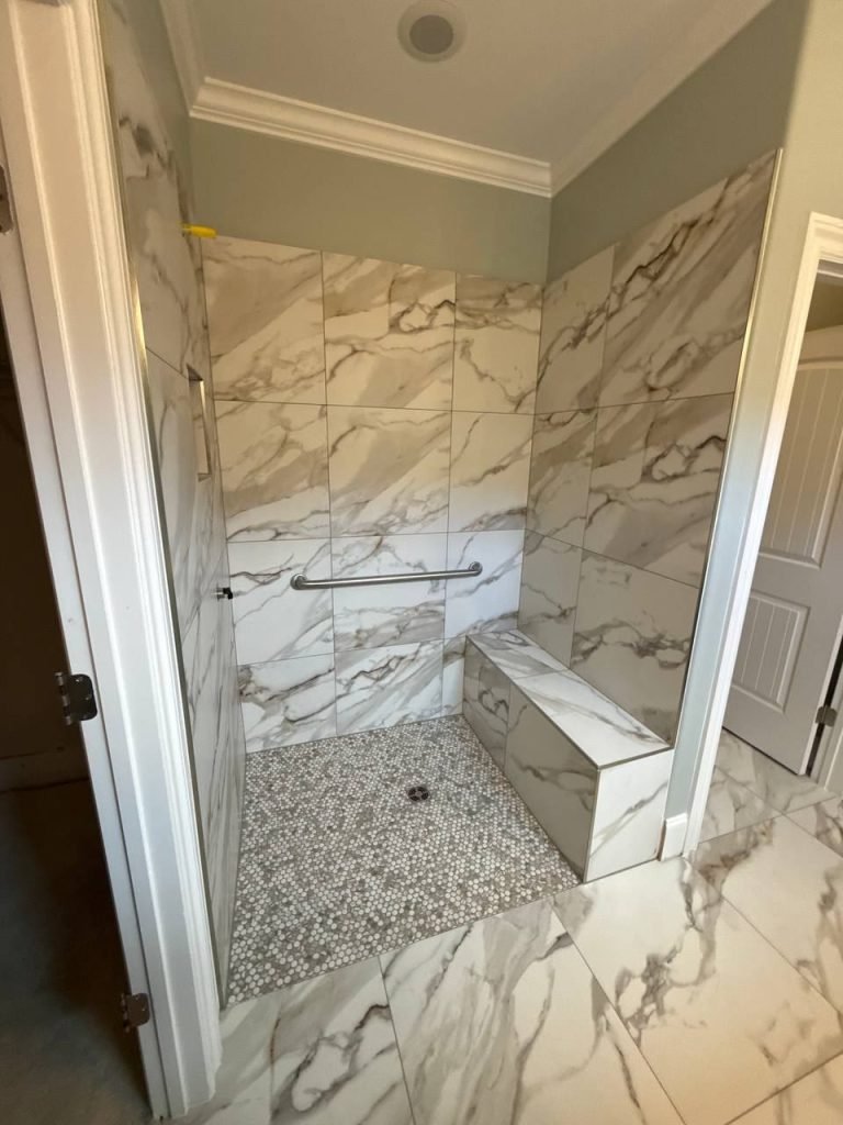 Finished shower in large-format marble-look tile with a mitred bench, penny-round mosaic floor and a grab bar.