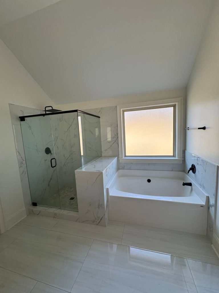 Restored bathroom with a frameless glass shower, marble-look tile surround and an alcove tub beneath a frosted window.