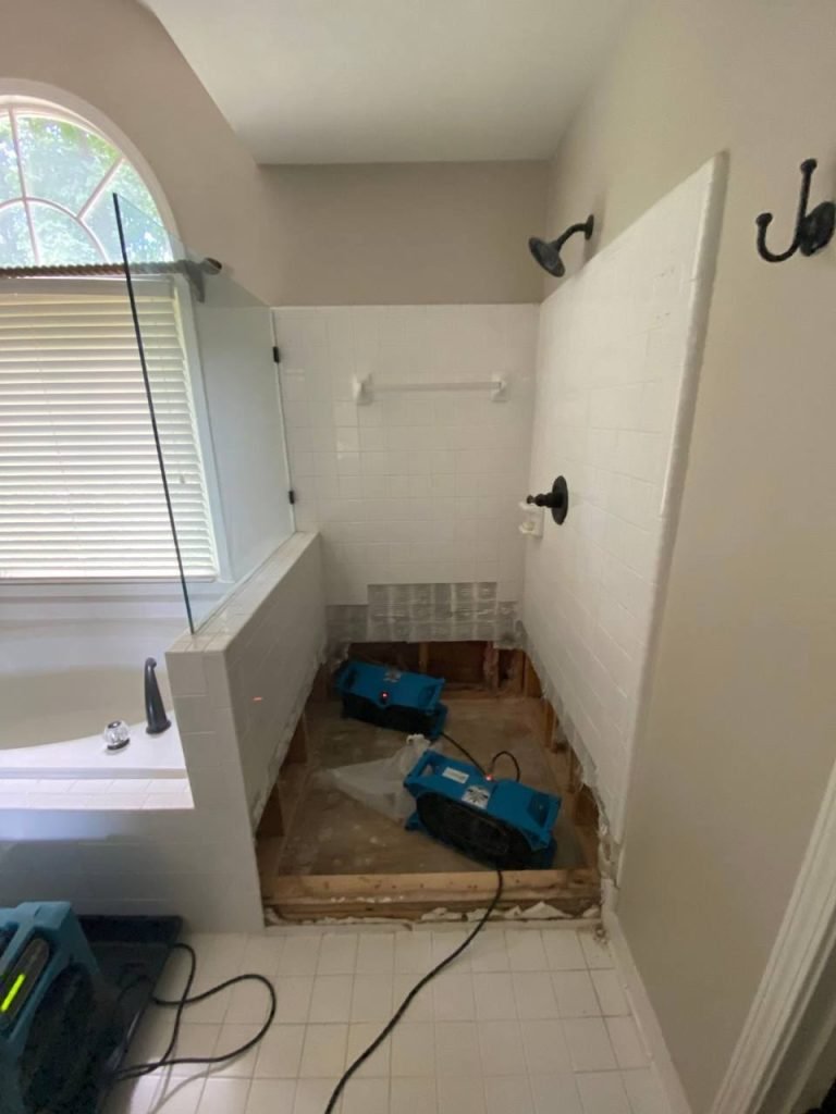 Air movers drying a bathroom after water damage, with tile and drywall removed to expose the subfloor.