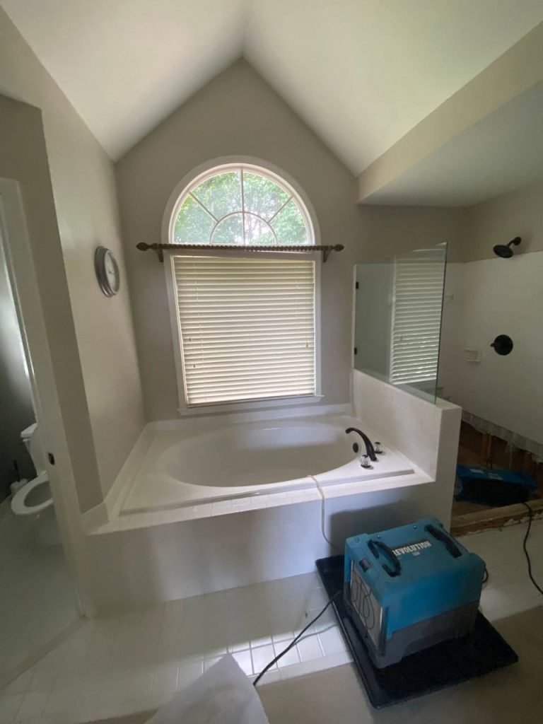Master bathroom before restoration: water-damaged flooring and old tub with drying equipment running.